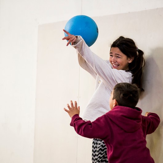 Girl holding blue ball laughing as boy tries to get the ball image