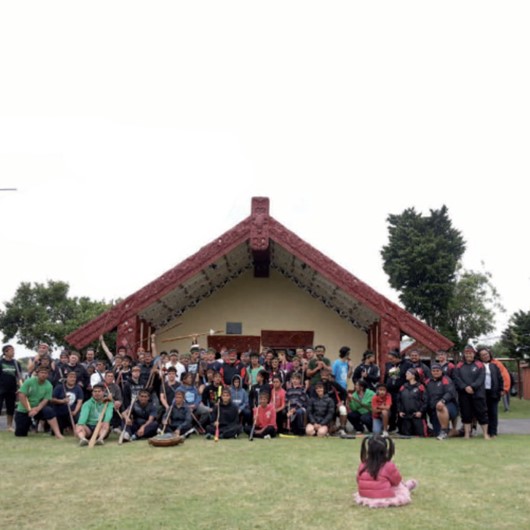 Teams pose for a photo in front of a marae image