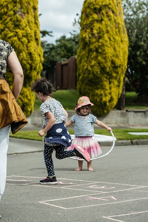 Pay streets event with two tamariki playing jump rope and hopscotch