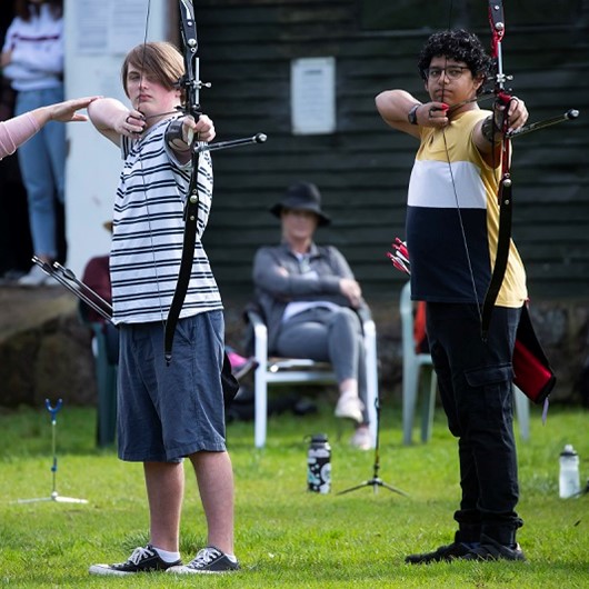 Two teenage boys pulling arrows at a target image