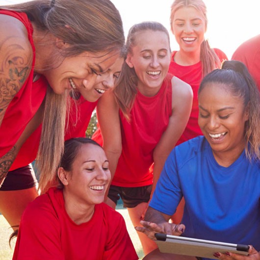 A team in red huddle around a person in blue with an ipad image