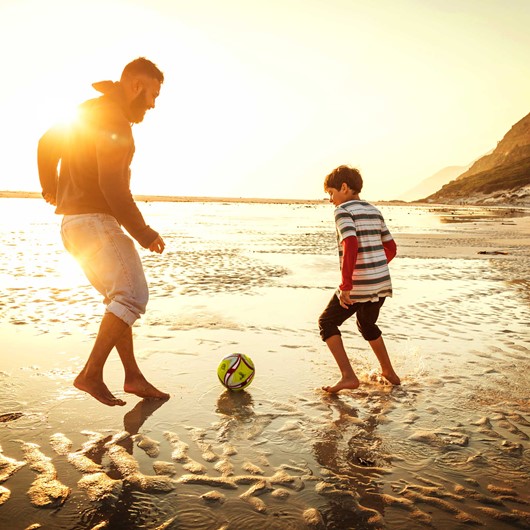 Adult and boy playing football on the beach