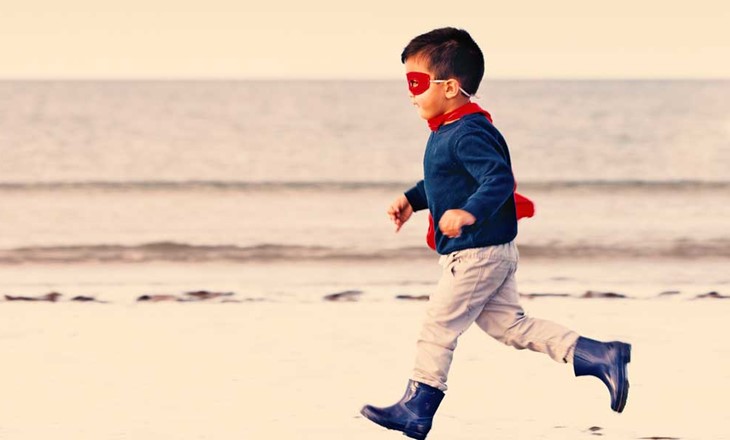 Young boy dressed as super hero running on beach
