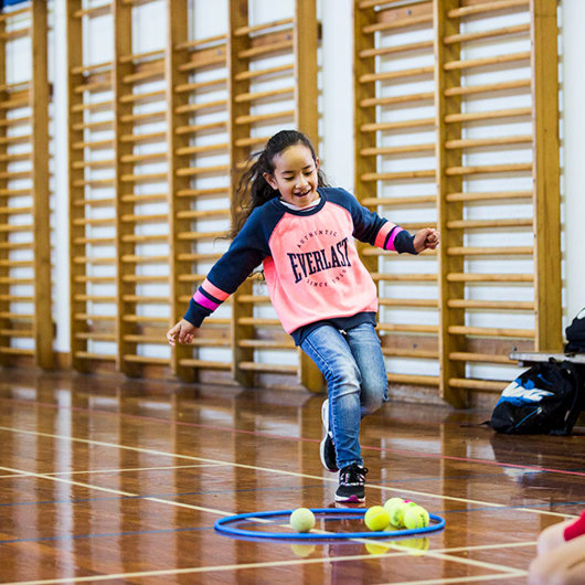 Girl in gym runs towards a hoop and tennis balls on ground image