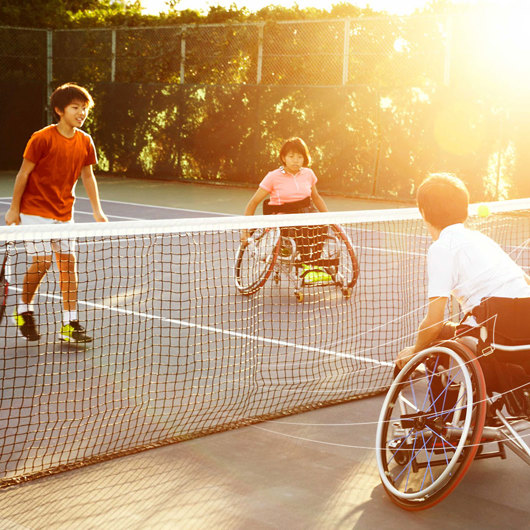 3 teens, 2 in wheelchairs playing tennis on a court