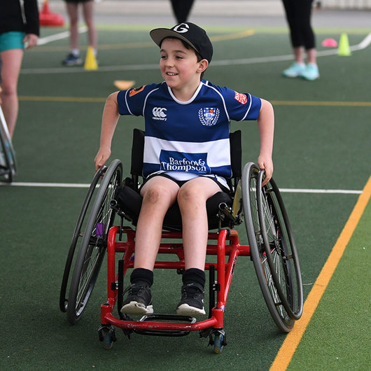 Smiling boy wheels his chair on a sports field image