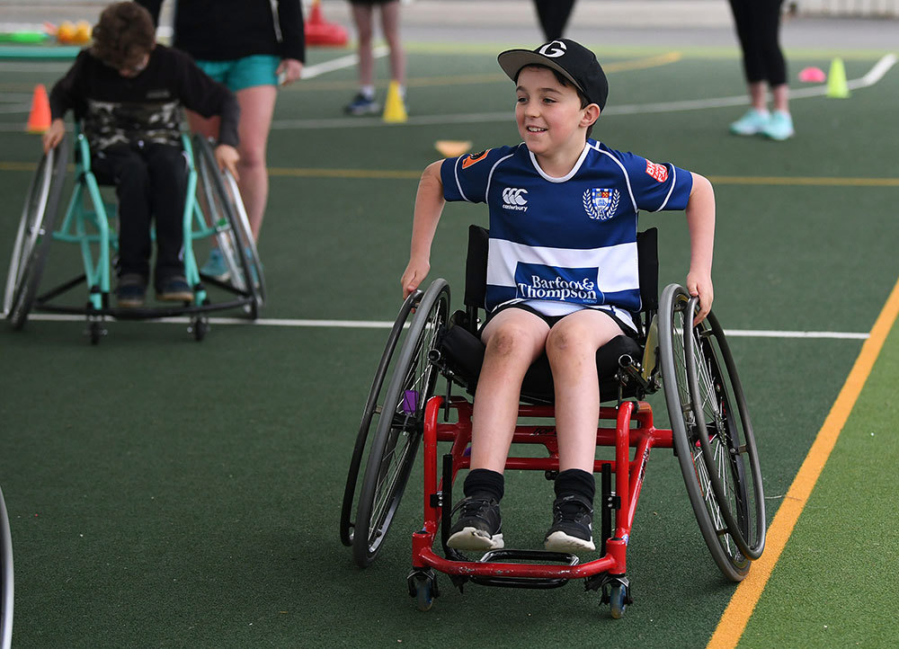 Smiling boy wheels his chair on a sports field