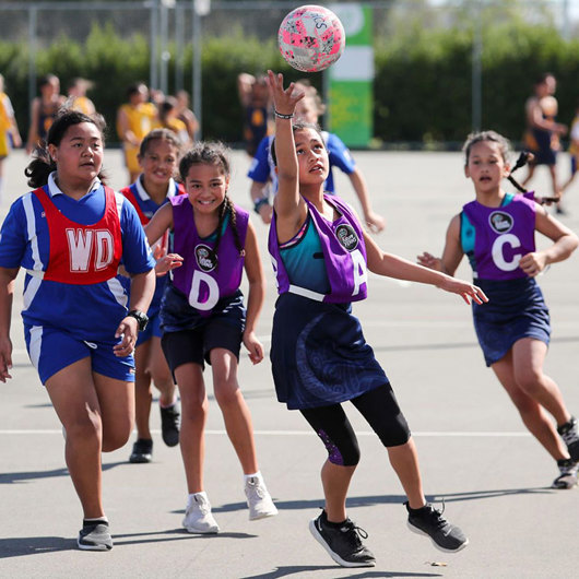 Girls in purple and red bibs playing netball