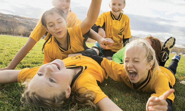 Tamariki In yellow uniforms relax on the field after a match