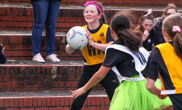 Girl in yellow bib looks for someone to pass netball to