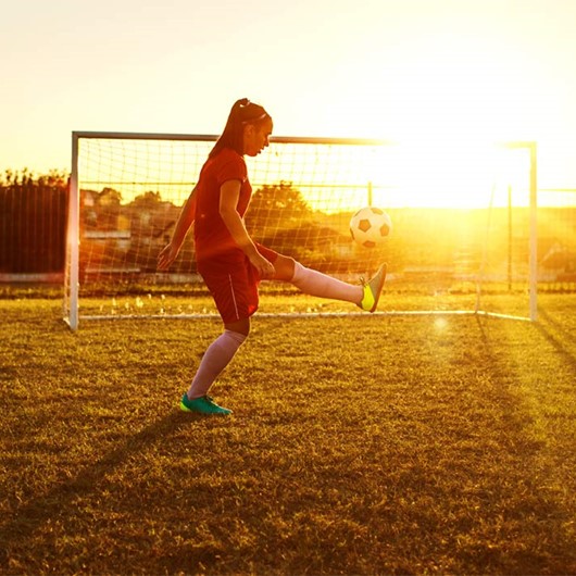 Girl keeps a football in the air on a football field