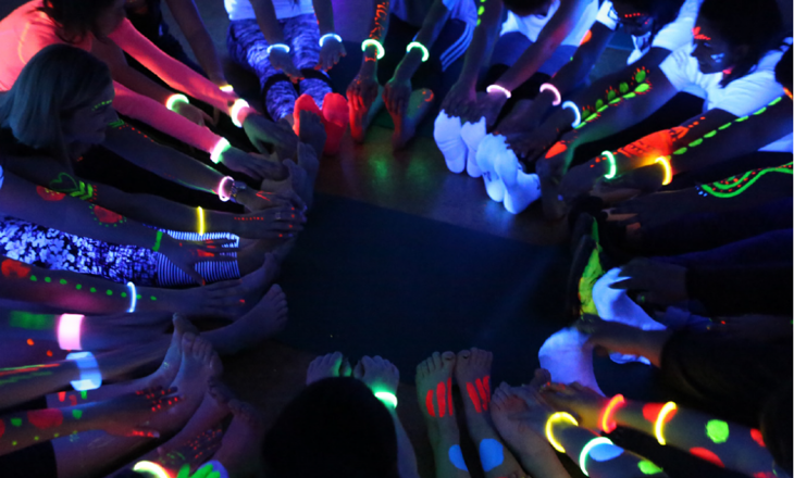 A circle of people stretching under uv lights wearing fluro