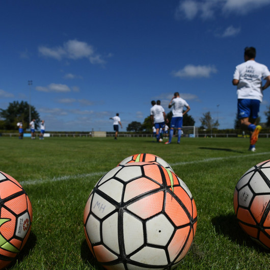 Closeup of three soccer balls with players and field behind image