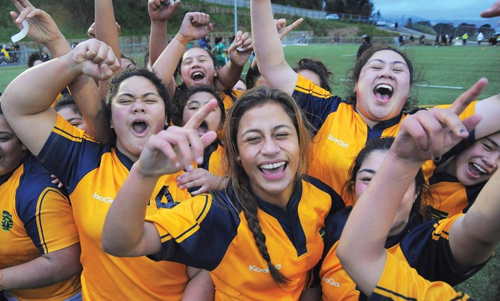 Girls rugby team smiling, cheering, and doing victory signs