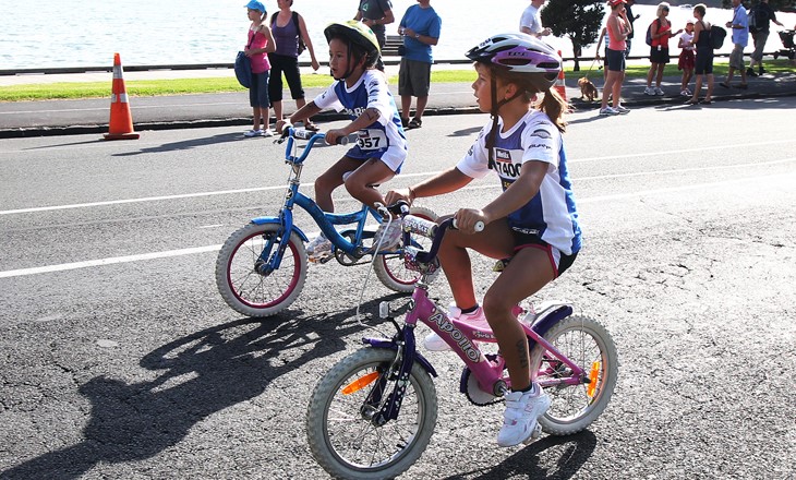 Two young tamariki on bikes cycling around a bay