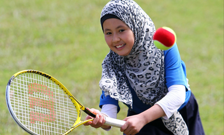 Smiling girl hits a tennis ball on a field