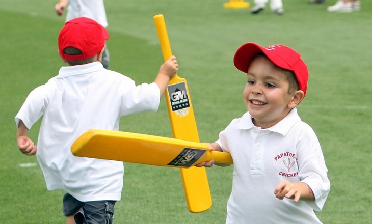young boys running with cricket bats on a field 