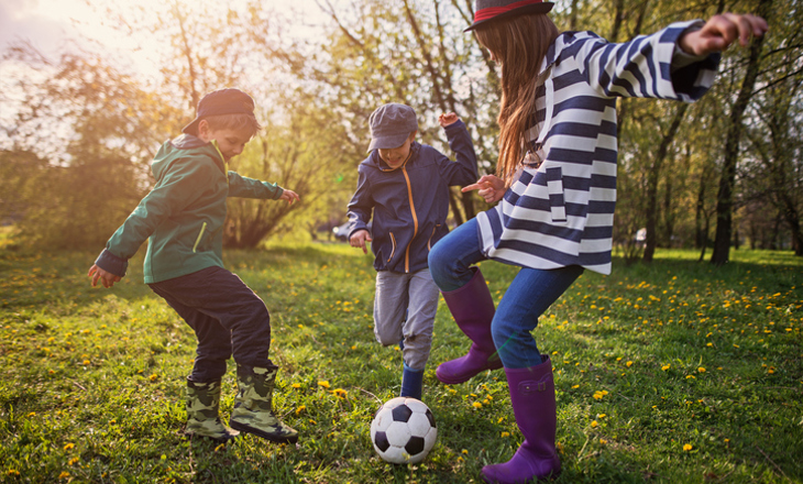 Three tamariki playing football outdoors