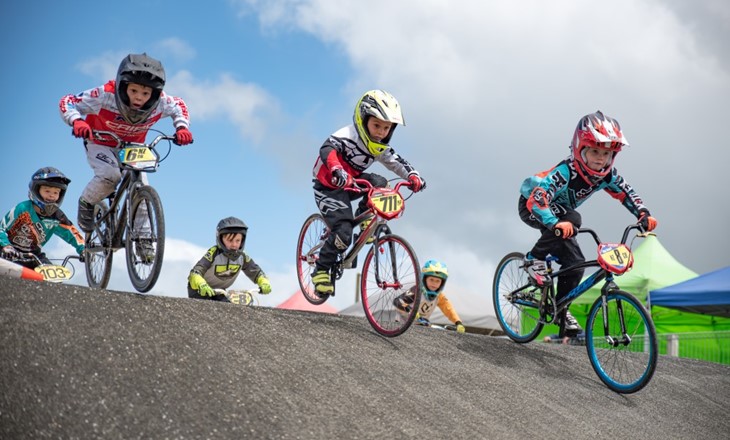 A group of kids in a BMX race coming over a hill