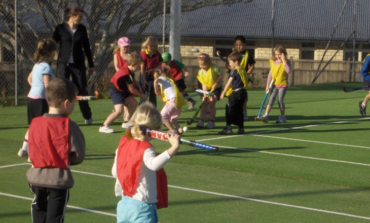 A dozen kids on a turf in teams playing hockey 