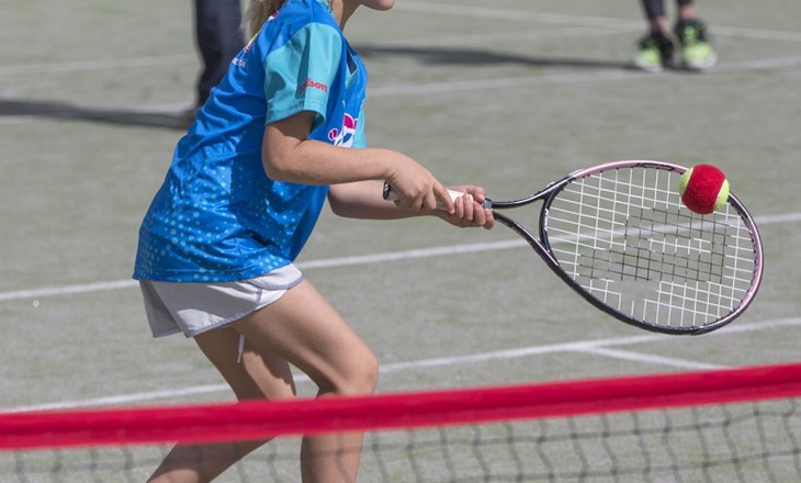 Young girl hitting a tennis ball on a tennis court 