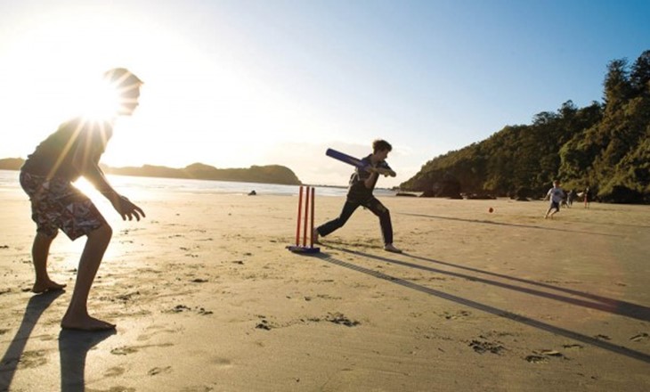 Two kids play beach cricket