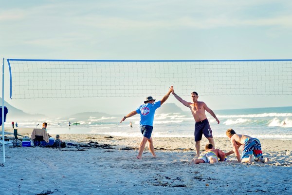 Two men high five on beach after beach volleyball match