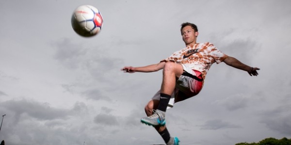 Asian teen kicking football high in the air