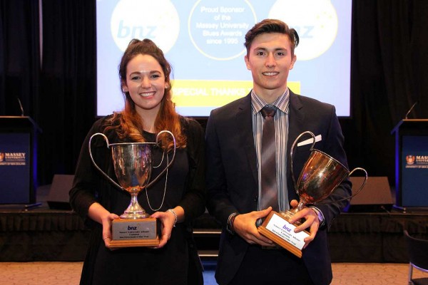 A young woman and young man each holding a large trophy