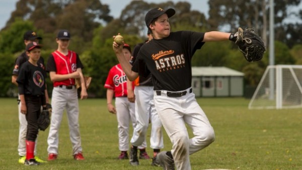 boy throwing ball as baseball team look on