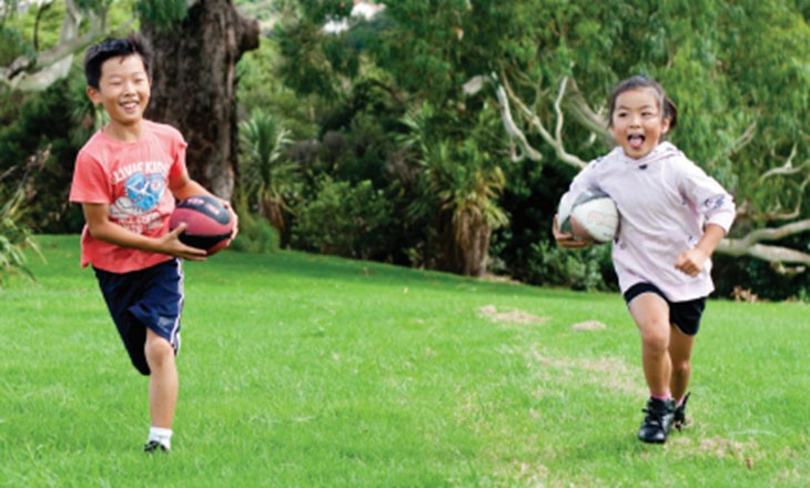 Smiling girl and boy each running carrying a rugby ball