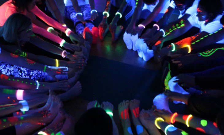 A circle of people stretching under uv lights wearing fluro