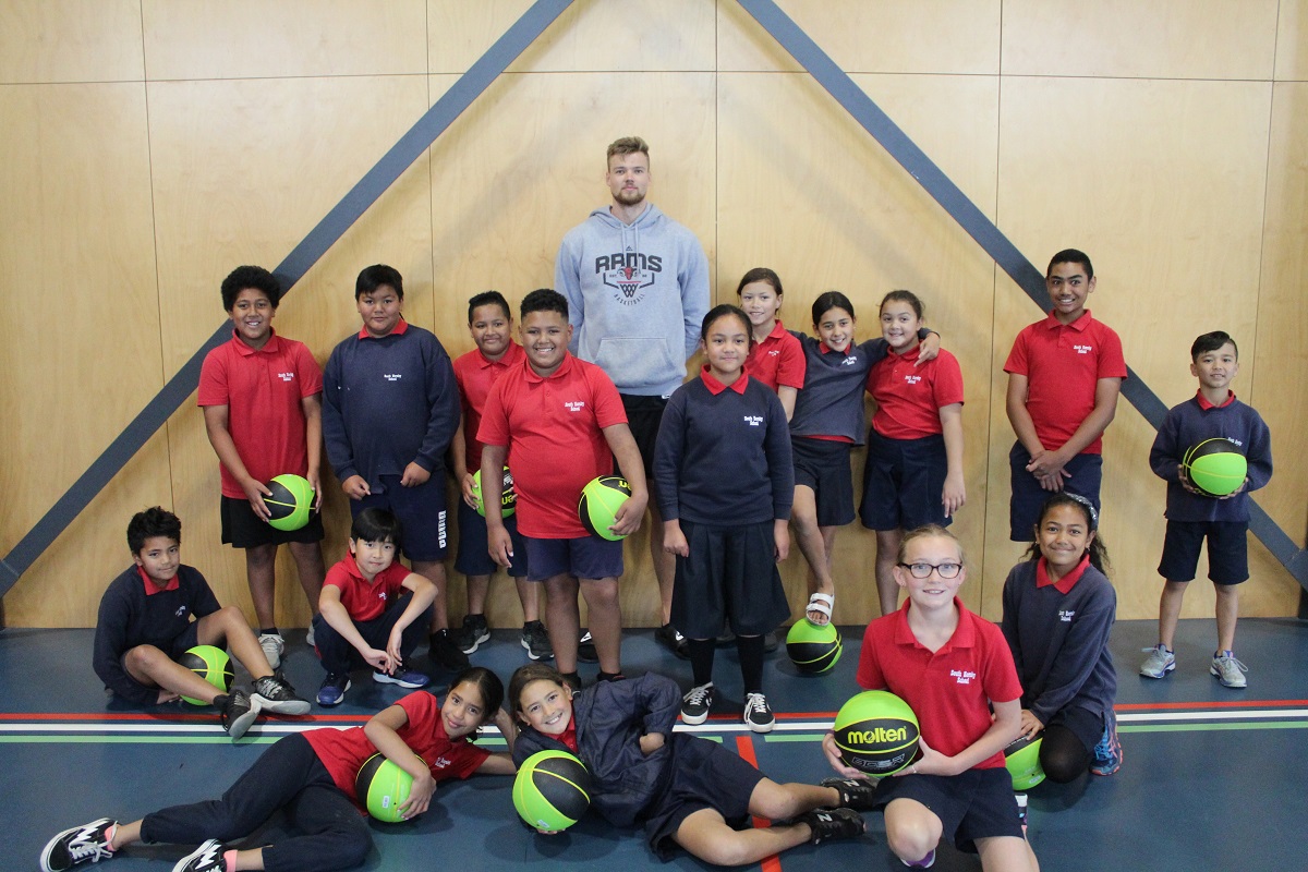 Group of tamariki standing against a wall with a Rams player