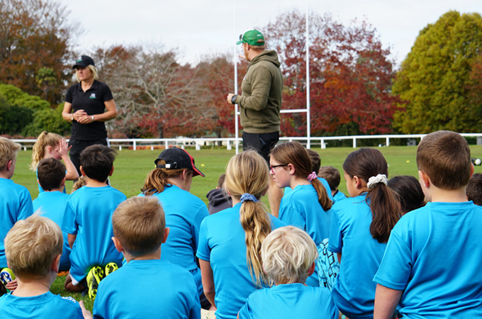 Students sit on a field listening to trainers