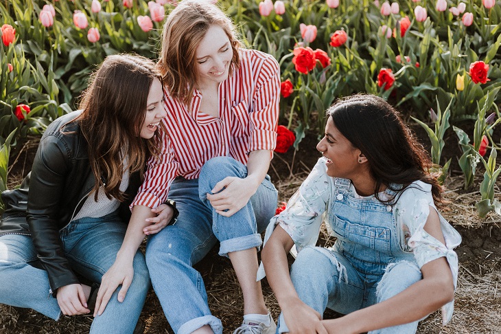 Group of 3 young women sitting in front of flowers chatting