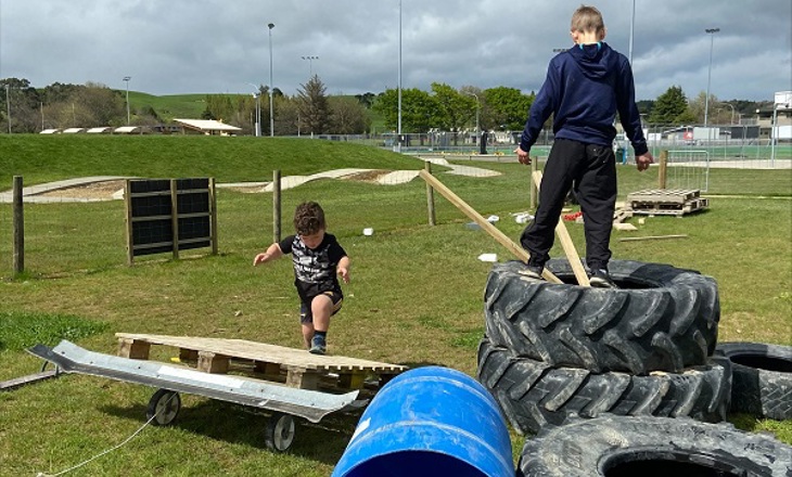 Two kids climbing over tyres and wooden pallets