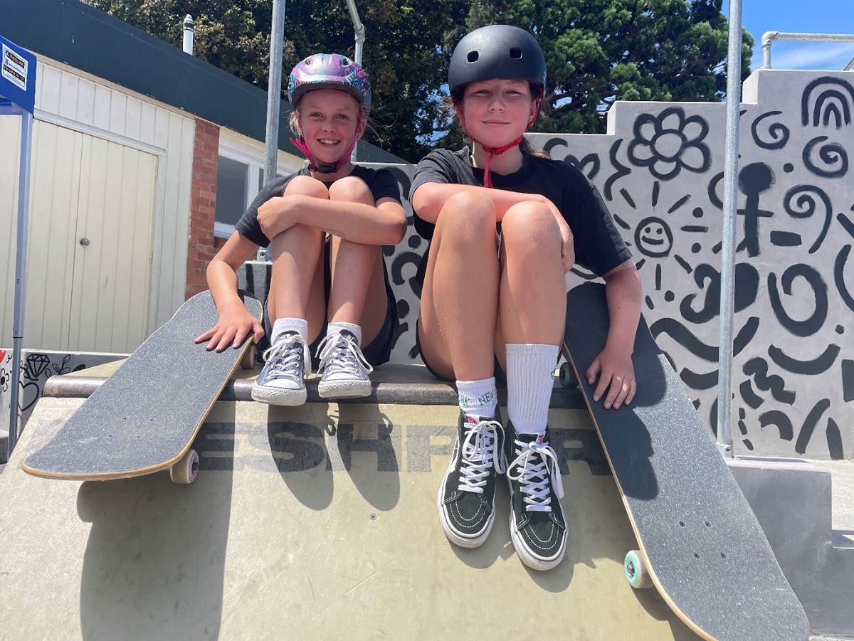Two young women sitting on top of a skateboard ramp