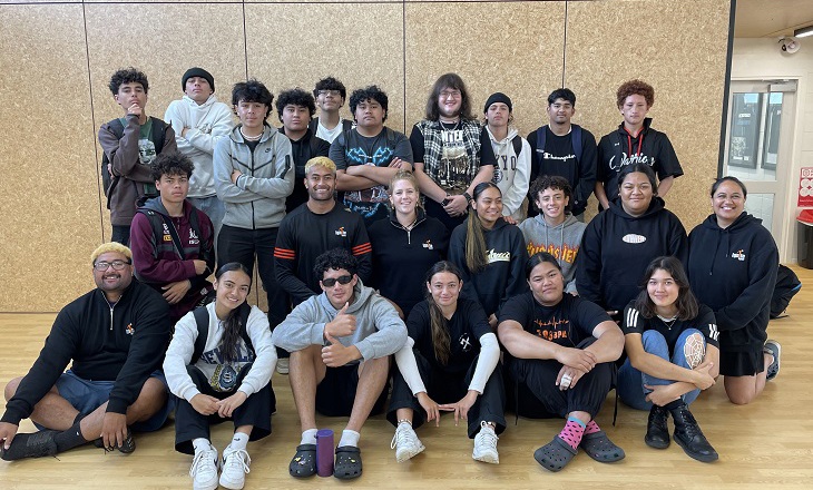 Group of rangatahi standing against a wall in a school hall