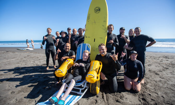 Group of people standing on a beach around a surfboard