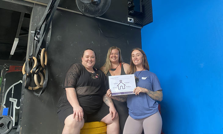 Three wahine holding a certificate in a weight training area