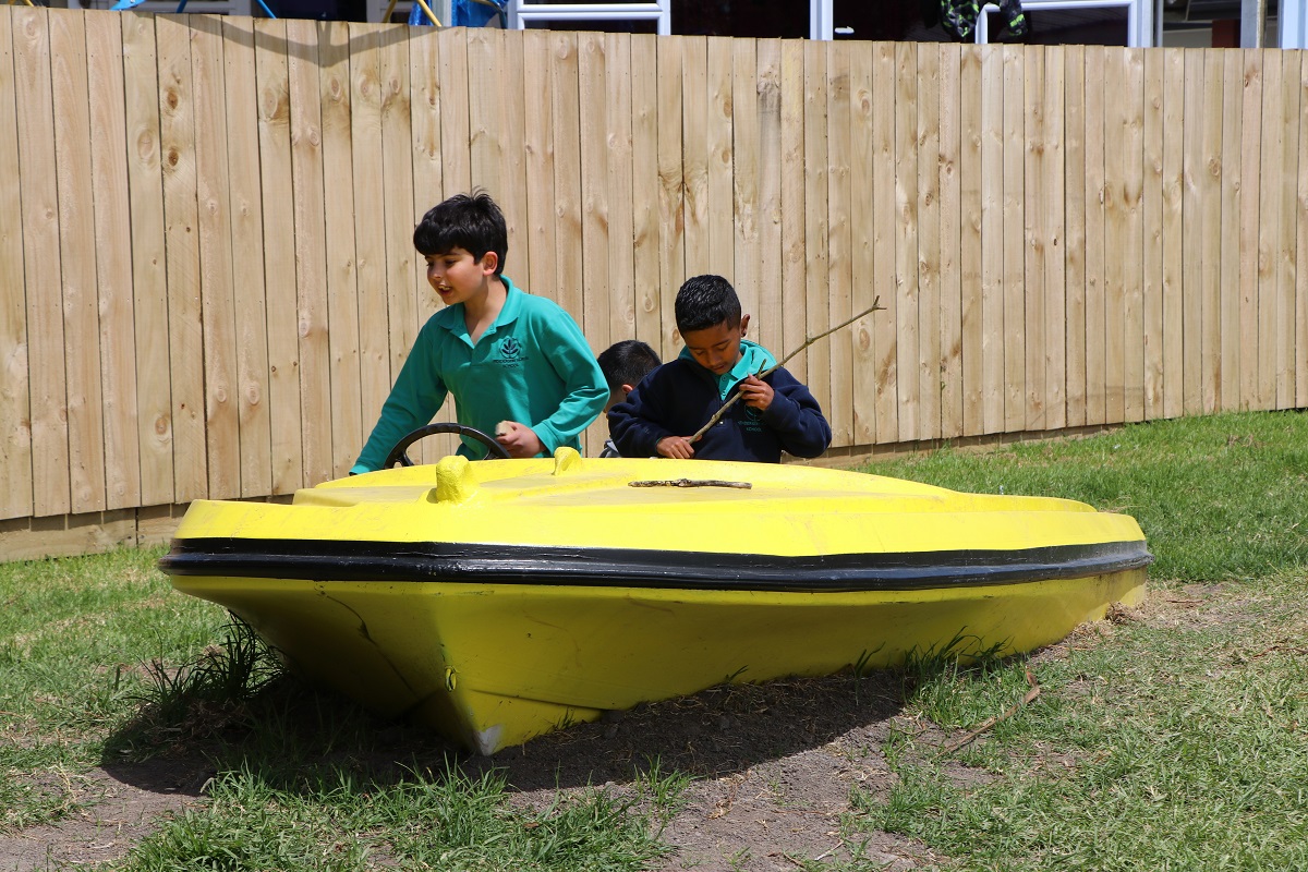 Three kids playing in a boat sitting on grass