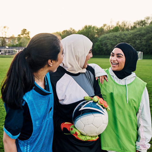 3 rangatahi young women enjoying a laugh with a football