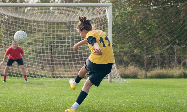 Young women kicking a soccer ball into a net 