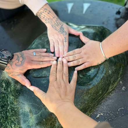 Four hands touching a large pounamu stone