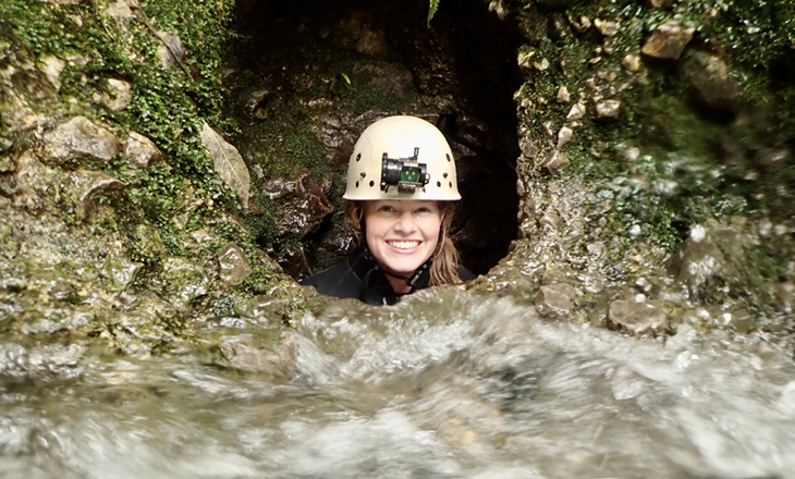 Caver peering out of a cave looking to the camera