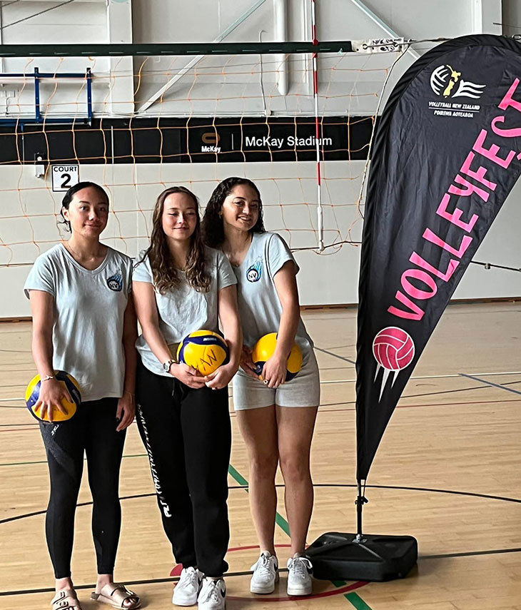 Three volleyball team mates on the court pose for a photo